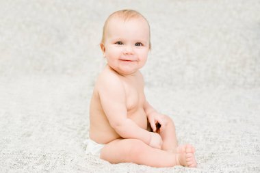 Mutlu bebek, yumuşak, nötr renkli battaniyeye oturmuş gülümsüyor ve kameraya bakıyor, masumiyet ve neşe dolu anları yakalıyor. Çocukluk, mutluluk, masumiyet ve aile hayatı kavramları için mükemmel..