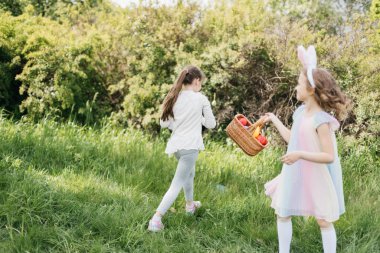 Paskalya yumurtası avı. Bahçede Paskalya yumurtası avında renkli yumurta toplamak için koşan tavşan kulaklı bir grup çocuk. Paskalya geleneği