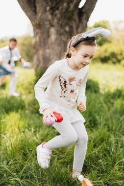 Paskalya yumurtası avı. Bahçede Paskalya yumurtası avında renkli yumurta toplamak için koşan tavşan kulaklı bir grup çocuk. Paskalya geleneği. Sepet bahar konseptiyle parkta gülen çocuklar.