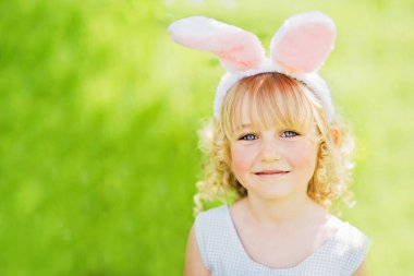 çocukluk, Paskalya kutlamaları, mevsimsel mutluluk, Paskalya yumurtası avı. Bahçede yumurta toplamak için koşan tavşan kulaklı bir kız çocuğu. Paskalya geleneği. Renkli yumurtalarla dolu sepeti olan bebek.