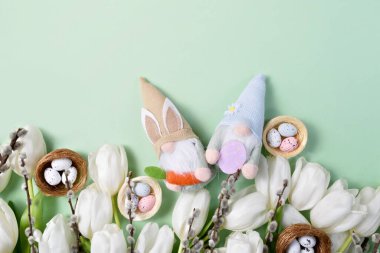 Easter Gnomes with White Tulips and Speckled Eggs in nests, and pussy willow branches on a pastel green background