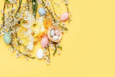 Çiçekli Bahar Kutlama Kartı ve Paskalya Yumurtaları Sarı Arkaplan. Renkli Paskalya yumurtaları, bahar çiçekleri ve parlak sarı arka planda yuva, neşeli tebrik kartı konsepti.