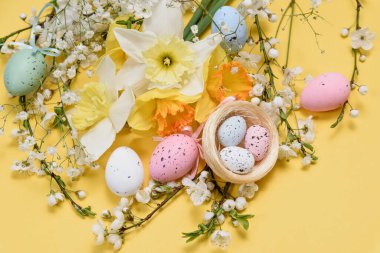 Çiçek aranjmanıyla bahar tatili kartı konsepti. Paskalya yumurtaları, bahar çiçekleri ve sarı arka planda dekoratif yuva. Parlak festival tasarımlı tebrik kartı kavramı.