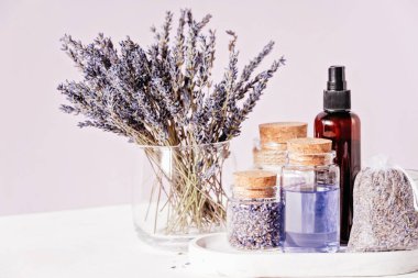 Lavanta ve Cam Kavanozlar 'ın oynadığı Spa ve Sağlık Sahnesi. Aromaterapi seansı. Cam bir vazoda kurumuş lavanta çiçekleri, mantar kapaklı şişeler, gerekli yağ, kese ve kehribar sprey şişesi.