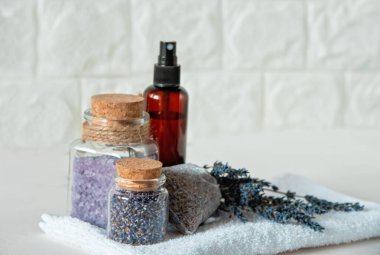 Kurumuş çiçek ve banyo tuzlu lavanta spa seti. Rahatlatıcı Spa Düzenlemesi. Lavanta çiçekleri, banyo tuzu, cam kavanozlarda kurutulmuş tomurcuklar, sprey şişesi ve beyaz havlunun üzerinde kese.