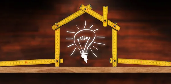 Folding ruler in the shape of a house and a design of a light bulb, above a wooden workbench with copy space.