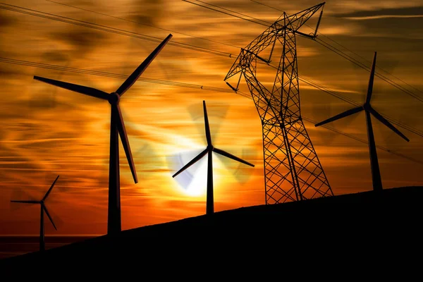 一组风力涡轮机和高压电塔的轮廓 电线和绝缘体在夕阳西下美丽天空中的轮廓 图库照片