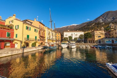 Malcesine köyü. Limanda küçük tekneler ve feribotlar demirli ve renkli evler var. Garda Gölü kıyısındaki ünlü turizm beldesi (Lago di Garda). Verona ili, Veneto, İtalya, Güney Avrupa.