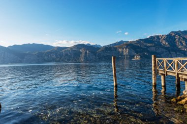 Garda Gölü kıyısındaki ahşap iskele (Lago di Garda) ve güney Avrupa 'daki Malcesine, Verona ilindeki küçük bir köyden İtalyan Alpleri manzarası. Lombardiya kıyılarında.