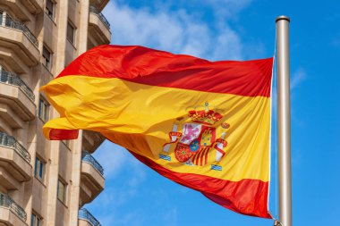 İspanya Meydanı (Plaza de Espana), Madrid, İspanya, Güney Avrupa 'da açık mavi gökyüzüne karşı rüzgarda dalgalanan bir İspanyol bayrağının yakın çekimi.