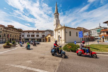 SPILIMBERGO, İtalya - 7 AUG 2022: 1536 'da çan kulesiyle San Rocco' nun küçük kilisesi. Spilimbergo, Pordenone, Friuli-Venezia Giulia, İtalya, Avrupa. Piaggio Vespa scooter kullanan bir grup motorcu..