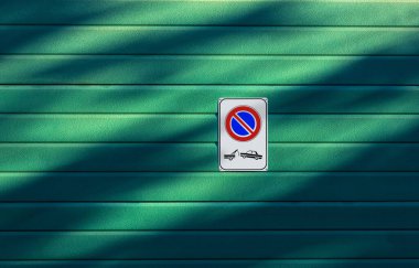 Closeup of a No Parking and Tow Away Zone sign on a green garage door, full frame, photography, Italy, Europe.