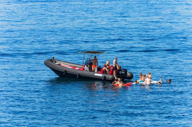 LA SPEZIA, ITALY - JULY 13, 2022: Motorized black dinghy and a group of people swimming in the sea on a sunny summer day, Mediterranean sea, Gulf of La Spezia, Liguria, Italy, Europe.