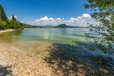 Beautiful beach of Lake Garda near the small town of Garda. Promontory of San Vigilio (Punta San Vigilio), Verona province, Veneto, Italy, Europe. On the horizon the hill called Rocca di Garda.
