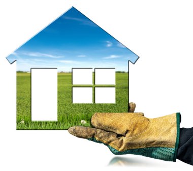 Closeup of a hand with protective work glove holding a small model house with a countryside landscape inside, isolated on white background.