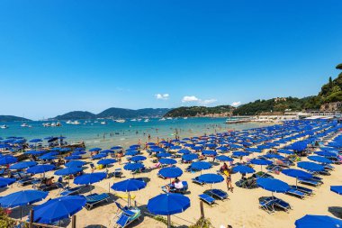 LERİKİ, İtalya - 16 Temmuz 2022: Mavi şemsiyeli Lerici Plajı, La Spezia Körfezi, Liguria, İtalya, Avrupa 'daki turizm beldesi. Arka planda San Terenzo ve Porto Venere adlı küçük bir köy var..