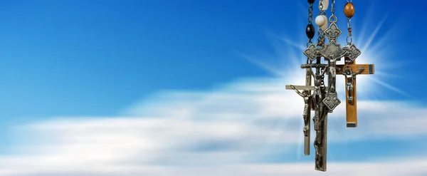雲とコピースペースを持つぼやけた澄んだ青い空に対して 金属と木製の十字架とロザリオビーズのグループのクローズアップ — ストック写真