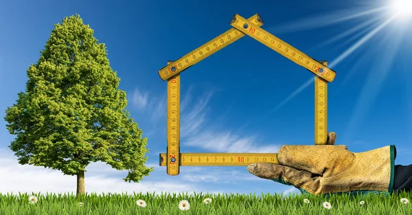 Design or project concept of an ecological house. Hand with work glove holding a folding ruler in the shape of a house, on a green meadow with flower and a green tree. Clear blue sky on background.