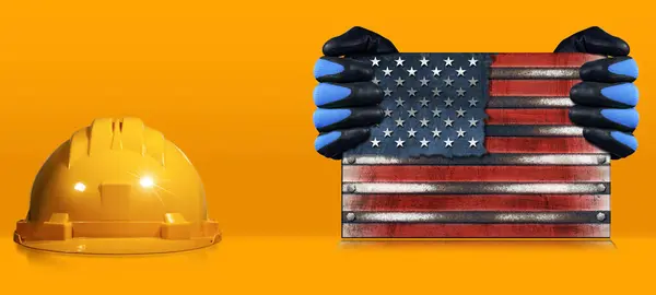 Happy Labor Day concept. Manual worker with work gloves holding a metal national flag of the United States of America, USA (American flag), on an orange background with a hardhat and copy space.