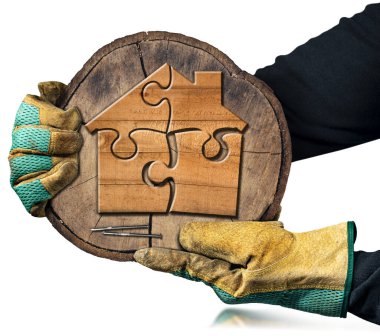 Ellerinde koruyucu iş eldivenleri olan eller yapboz parçalarından oluşan küçük ahşap bir evle bir ağaç gövdesinin bir kesitini tutuyor. Beyaz arka planda izole edilmiş. İnşaat endüstrisi konsepti.