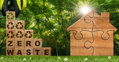 Gloved hand arranging wood blocks with text Zero Waste and Recycling Symbols on a green meadow with a small wooden house made of jigsaw puzzle pieces. Green forest on background. clipart