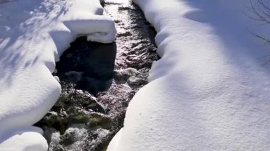 Harika bir kış masalı. Karlı bir orman, bir dağ nehri, dağların üzerinde güneş. Doğa manzarası. Güneş ışınları merceğe güzelce düşer. Kamera aşağıdan yukarıya hareket eder