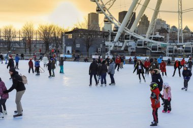 Montreal turizmi. Dönme dolabın yanında kış buz pateni pisti. İnsanlar kışın gün batımının arka planında kayıyorlar.. 