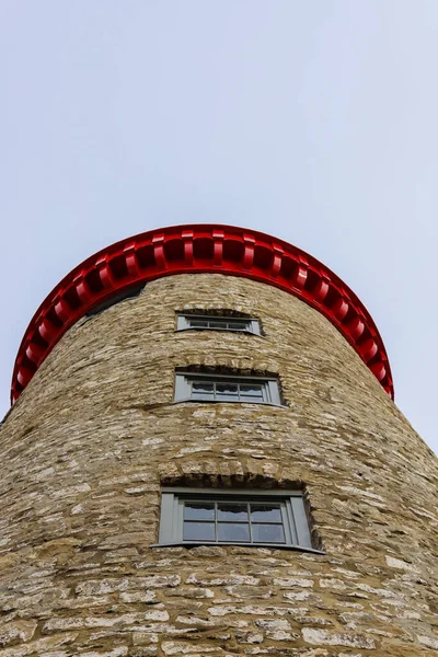 Old stone lighthouse - details. Red roof, wooden windows and natural stone wall.