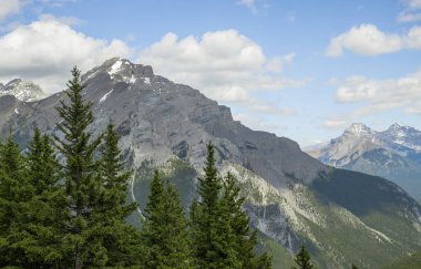Dağ manzarası - kozalaklı orman, bulutlu güzel mavi gökyüzü. Doğada yaz turizmi. Banff, Alberta, Kanada. Rocky Dağları