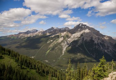 Mountain peaks of the Rocky Mountains in summer. Natural landscape background. Coniferous forest, remnants of snow. blue sky and clouds. Tourist season in Banff, Canada