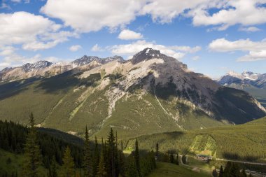 Mountain peaks of the Rocky Mountains in summer. Natural landscape background. Coniferous forest, remnants of snow. blue sky and clouds. Tourist season in Banff, Canada