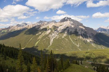 Mountain peaks of the Rocky Mountains in summer. Natural landscape background. Coniferous forest, remnants of snow. blue sky and clouds. Tourist season in Banff, Canada