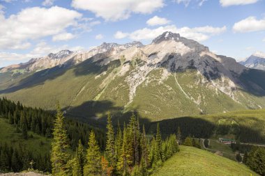 Mountain peaks of the Rocky Mountains in summer. Natural landscape background. Coniferous forest, remnants of snow. blue sky and clouds. Tourist season in Banff, Canada