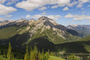 Mountain peaks of the Rocky Mountains in summer. Natural landscape background. Coniferous forest, remnants of snow. blue sky and clouds. Tourist season in Banff, Canada