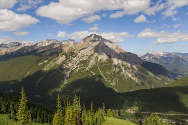 Mountain peaks of the Rocky Mountains in summer. Natural landscape background. Coniferous forest, remnants of snow. blue sky and clouds. Tourist season in Banff, Canada