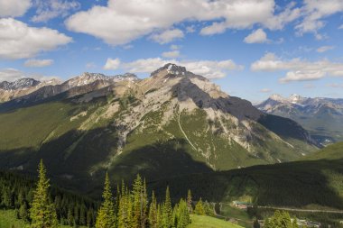 Mountain peaks of the Rocky Mountains in summer. Natural landscape background. Coniferous forest, remnants of snow. blue sky and clouds. Tourist season in Banff, Canada