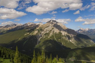 Mountain peaks of the Rocky Mountains in summer. Natural landscape background. Coniferous forest, remnants of snow. blue sky and clouds. Tourist season in Banff, Canada