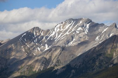 Mountain peaks of the Rocky Mountains in summer. Natural landscape background. Coniferous forest, remnants of snow. blue sky and clouds. Tourist season in Banff, Canada
