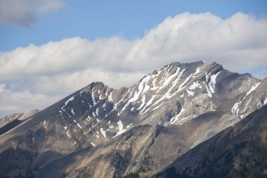 Mountain peaks of the Rocky Mountains in summer. Natural landscape background. Coniferous forest, remnants of snow. blue sky and clouds. Tourist season in Banff, Canada