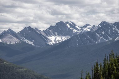 Güneşli bir günde güzel dağ manzarası - Banff İl Parkı, Rocky Dağları, Alberta, Kanada 'daki dağ zirveleri, güneş ışınları ve kozalaklı orman