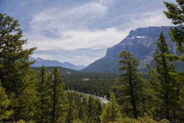 Güneşli bir günde güzel dağ manzarası - Banff İl Parkı, Rocky Dağları, Alberta, Kanada 'daki dağ zirveleri, güneş ışınları ve kozalaklı orman