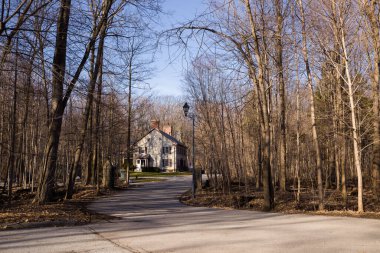 Baharın başında parkta pencereleri panjurlu bir bacası olan eski bir ev. Bahar sezonu. Güneşli bir gün. Eve giden dolambaçlı yol.