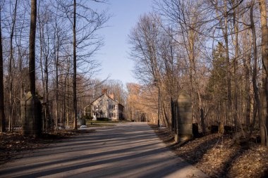 Baharın başında parkta pencereleri panjurlu bir bacası olan eski bir ev. Bahar sezonu. Güneşli bir gün. Eve giden dolambaçlı yol.