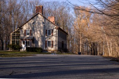 Baharın başında parkta pencereleri panjurlu bir bacası olan eski bir ev. Bahar sezonu. Güneşli bir gün. Eve giden dolambaçlı yol.