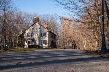 Baharın başında parkta pencereleri panjurlu bir bacası olan eski bir ev. Bahar sezonu. Güneşli bir gün. Eve giden dolambaçlı yol.