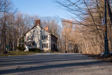 Baharın başında parkta pencereleri panjurlu bir bacası olan eski bir ev. Bahar sezonu. Güneşli bir gün. Eve giden dolambaçlı yol.