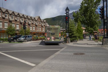 Toplu taşıma - Banff 'ta elektrikli şehir otobüsü. Dağlarda Alberta Turizmi. Şehir merkezinde evler, otobüs durağı ve arka planda dağ var.