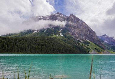 Banff Ulusal Parkı, Alberta, Kanada 'daki Muhteşem Louise Gölü. Yağmurdan sonraki gün bulutlu. Mavi göl suyu ve sisli tepeler. Seyahat için ünlü bir yer. Idyllic yaz manzarası. 
