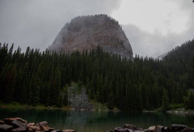 Kanada Rocky Dağları 'nda, Alberta' da, Kanada turizminde çok güzel bir zümrüt yeşili dağ gölü. Yağmurlu bir gün, sis, ağaçların arasından geçen bulutlar. Temiz sakin su, ıslak hava. Ayna Gölü 'nün taşlı kıyıları.
