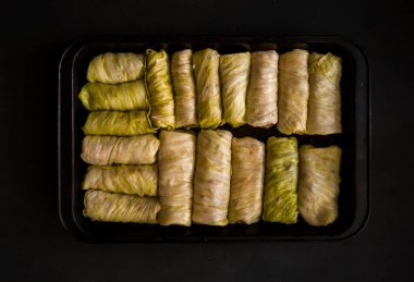 Siyah arka planda fırın tepsisine doldurulmuş lahana ruloları. Seçici odaklanma. Ton halinde. Ukrayna geleneksel yemeği. Doğu Avrupa mutfağı. Üst görünüm, kopyalama alanı ile.